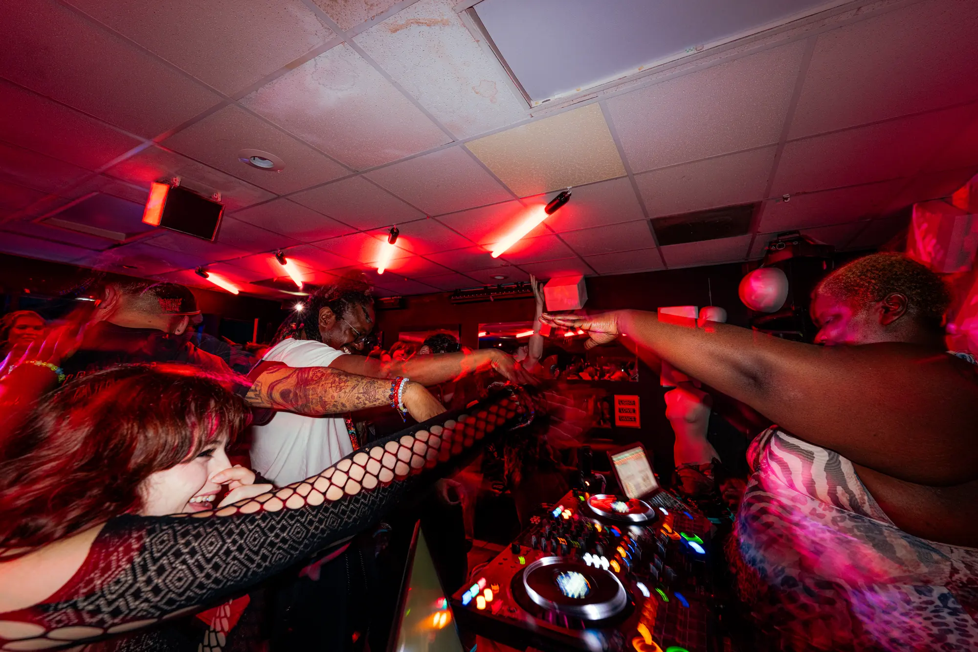 The DJ leans over the booth for a fist bump with a dancer in the front row