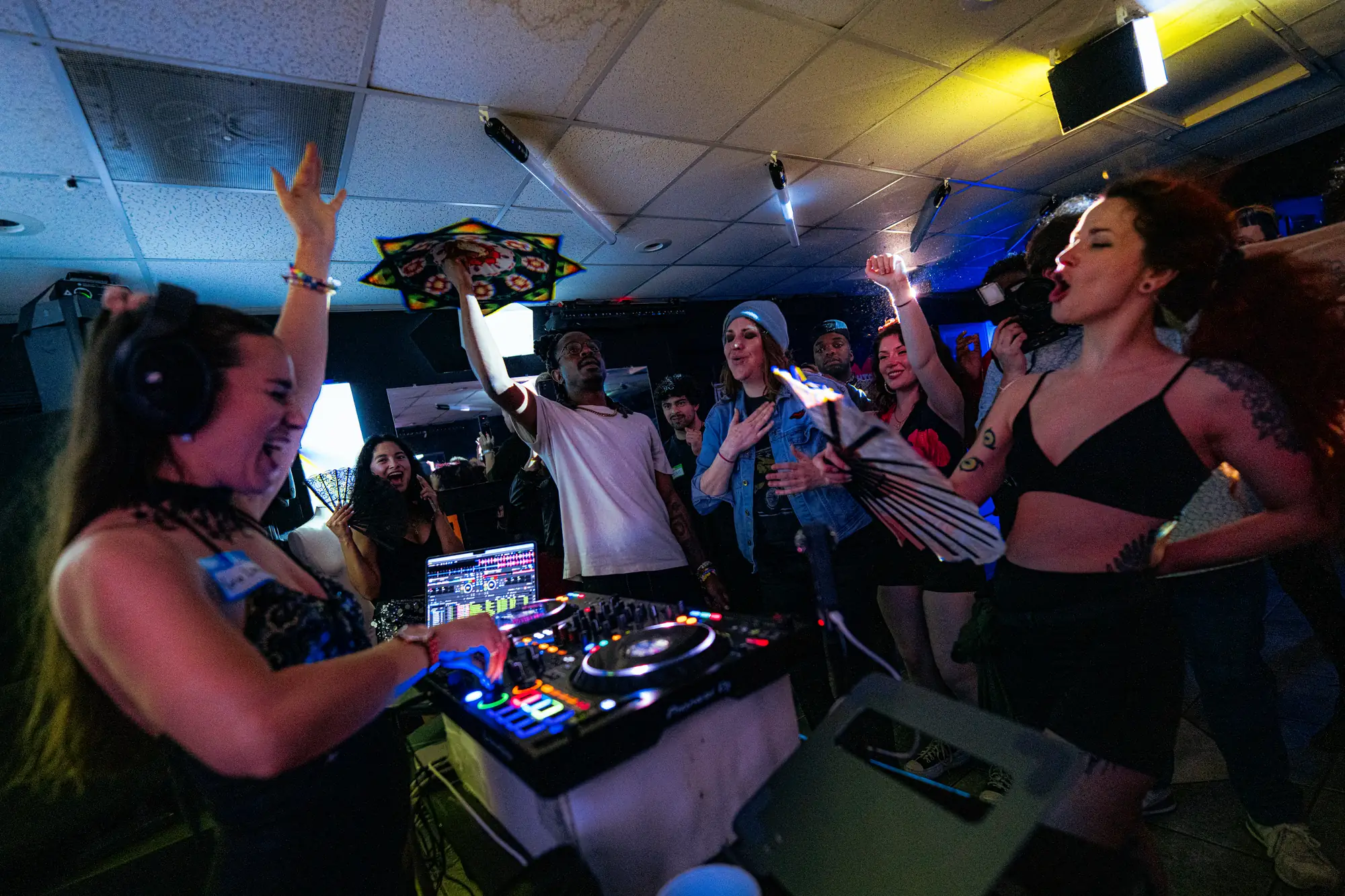 The DJ stands up on the booth as the floor surges below